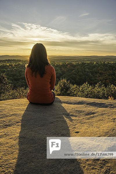 Frau sitzt auf einer Klippe mit Blick auf den Algonquin Park im Herbst bei Sonnenuntergang; Ontario  Kanada'.
