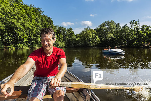 'A man wearing a red shirt rowing a boat down a calm river on a clear  sunny day; Darmstadt  Hessen  Germany'