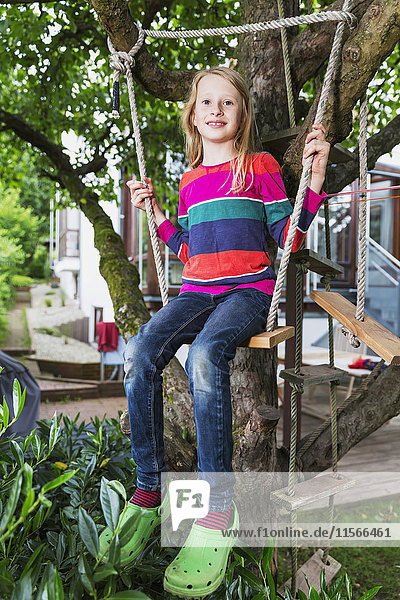 'Portrait of a young girl sitting on a tree swing in her backyard; Darmstadt  Hessen  Germany'
