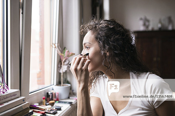 Woman doing her makeup by the window.