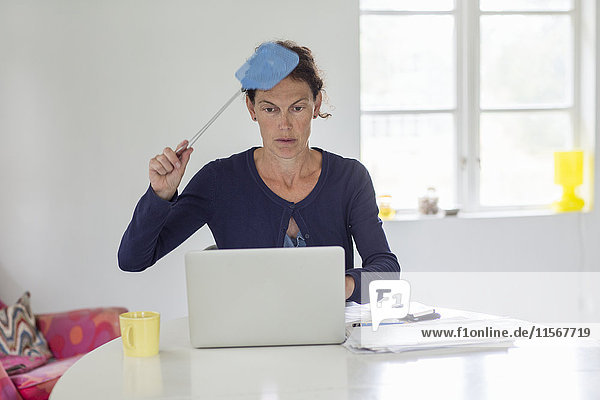 Frau sitzt vor einem Laptop und hält eine Fliegenklatsche
