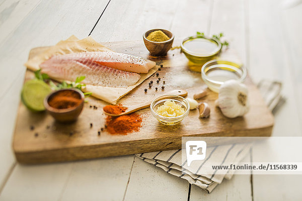 Raw tilapia and ingredients on cutting board