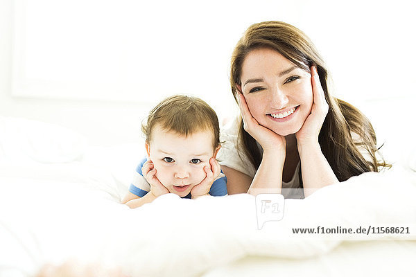 Mother and son (4-5) lying on bed and smiling