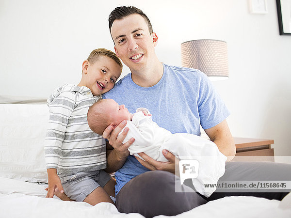 Father carrying daughter (0-1 months) and sitting on bed with son (4-5)