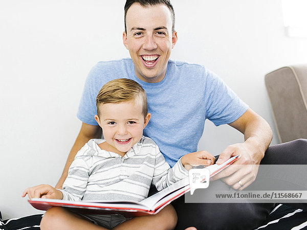 Father and son (4-5) sitting on bed and holding book