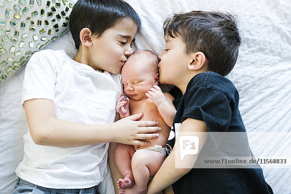 Two boys (6-7  8-9) kissing baby brother (2-5 months)