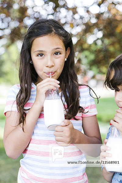 Mädchen (10-11) und Junge (6-7) trinken im Park Milch