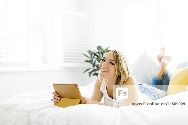 Frau mit digitalem Tablet auf dem Bett liegend