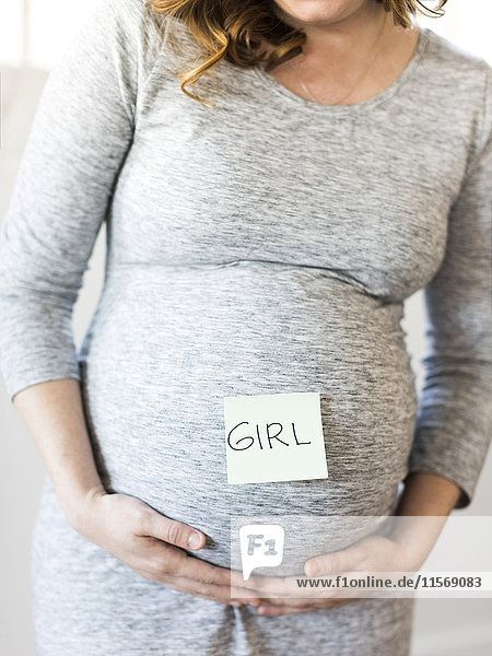 Porträt einer lächelnden schwangeren Frau mit Haftnotiz auf dem Bauch
