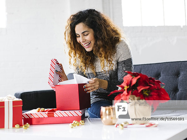Glückliche Frau auf dem Sofa beim Öffnen eines Weihnachtsgeschenks