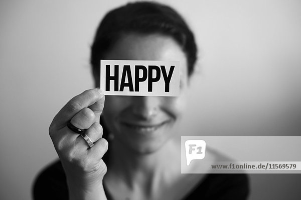 Porträt einer lachenden Frau  hält Karte mit Aufschrift Happy