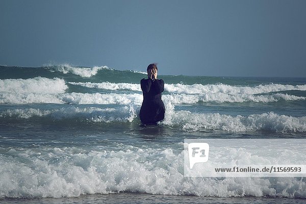 Woman in black dress with mask  standing in the surf in the sea