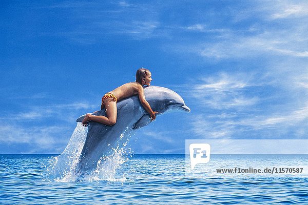 Six year old girl riding a dolphin leaping out of the sea  Corsica  France  Europe