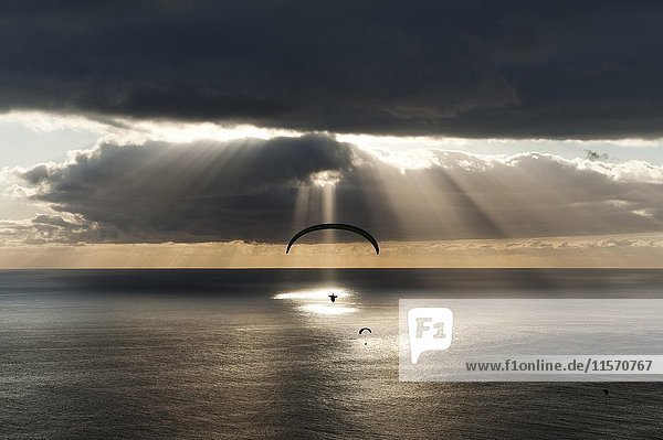 Sonne strahlt hinter dunklen Wolken mit Gleitschirm über dem Atlantik Puerto Naos Kanareninsel La Palma Spanien Europa