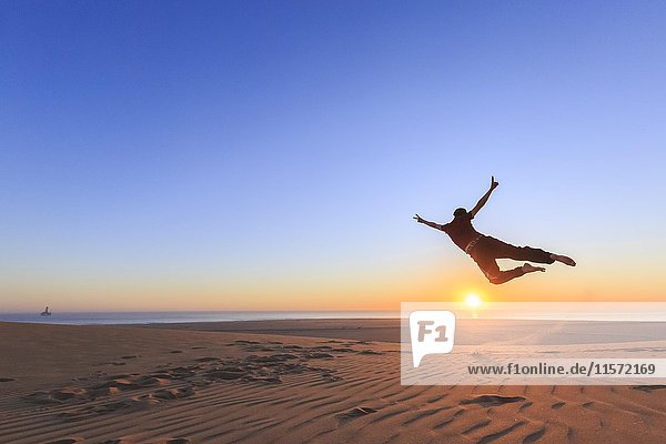 Junger Mann springt fröhlich in die Luft  Sonnenuntergang  Namib-Wüste  Langstrand  Swakopmund  Erongo-Region  Namibia  Afrika