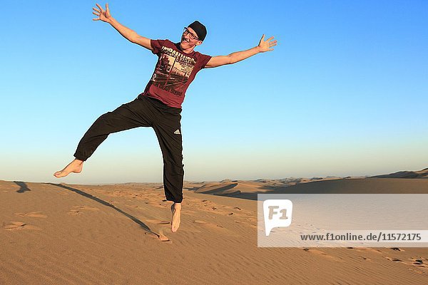 Junger Mann springt fröhlich in die Luft  Namib-Wüste  Langstrand  Swakopmund  Erongo-Region  Namibia  Afrika