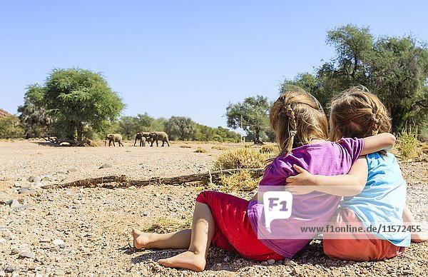 Zwei Mädchen beobachten Elefanten (Loxodonta africana) im Flussbett des Aba Huab  Damaraland  Kunene Region  Namibia  Afrika