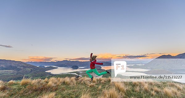 Wanderer springt in die Luft  Blick auf Lake Wanaka und Berge  Sonnenuntergang  Rocky Peak  Glendhu Bay  Otago  Southland  Neuseeland  Ozeanien