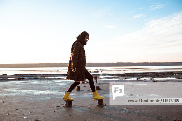 Woman balancing on wooden stumps on beach