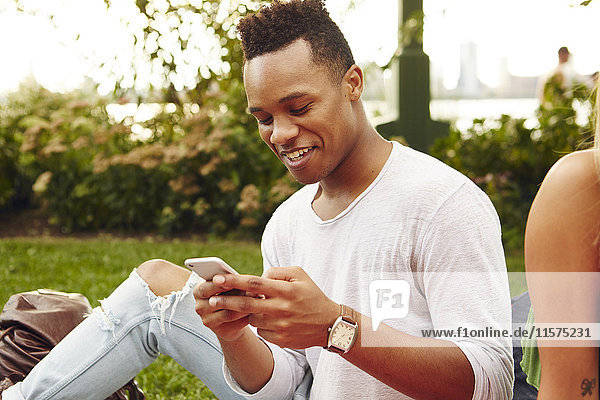 Young man looking at smartphone sitting in park