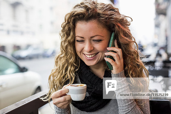 Frau im Café mit Espressotasse und lächelndem Telefonanruf