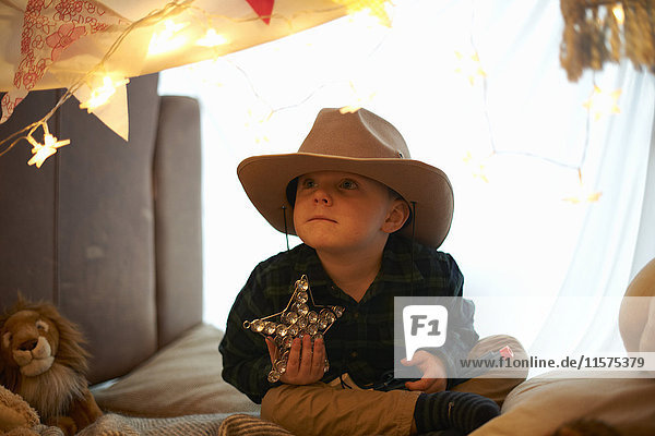 Porträt eines süßen Jungen mit Cowboyhut  der einen Stern in der Schlafzimmerhöhle hält