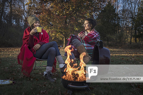 Two female friends wrapped in blankets by campfire