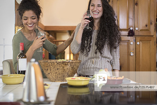 Zwei Freundinnen bereiten Salat zu und lachen an der Küchentheke