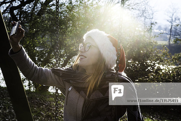 Junge Frau trägt  im Freien  trägt Weihnachtsmütze  nimmt Selfie mit Smartphone