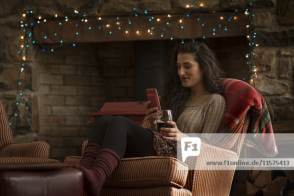 Young woman relaxing in armchair reading smartphone texts