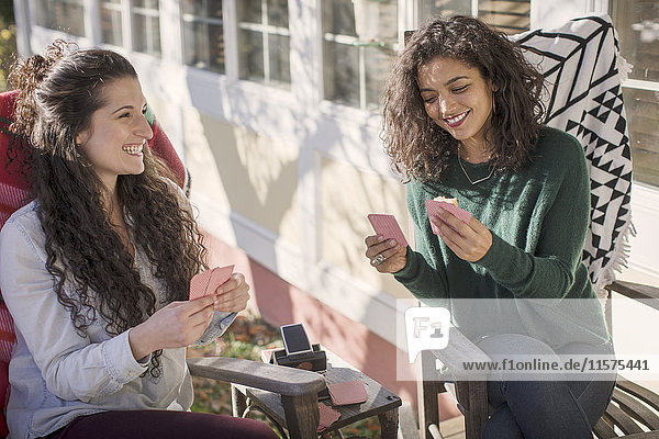 Zwei junge Freundinnen  die lachen und Kartenspiel auf der Terrasse spielen.