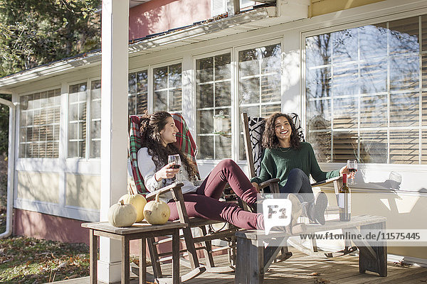 Zwei junge Freundinnen entspannen auf der sonnigen Terrasse bei Rotwein