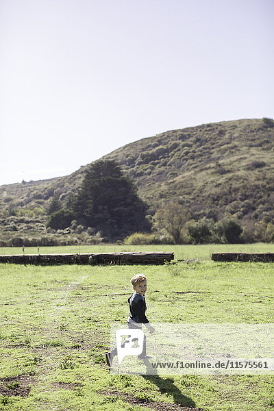 Boy running across green  hill in background