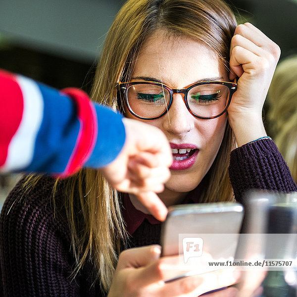 Young woman with boy's hand pointing at smartphone in cafe