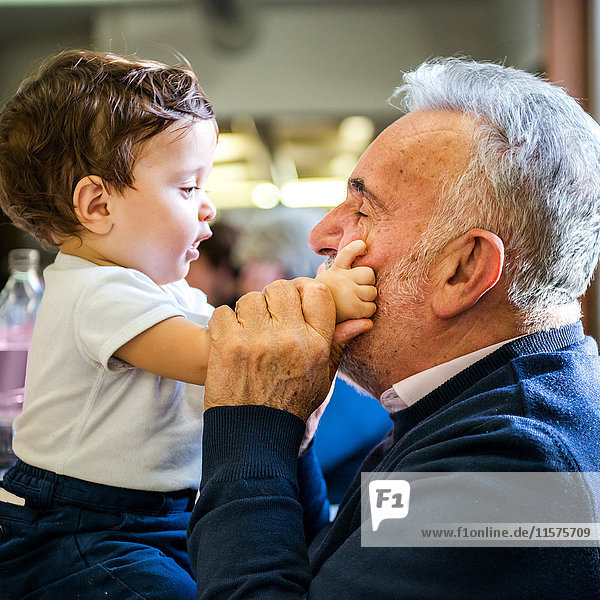 Senior man face to face with baby grandson in cafe