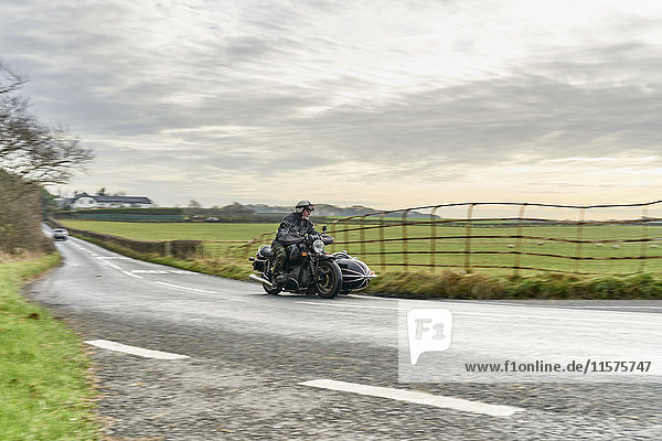 Älterer Mann und Enkel fahren Motorrad und Beiwagen auf einer Landstraße