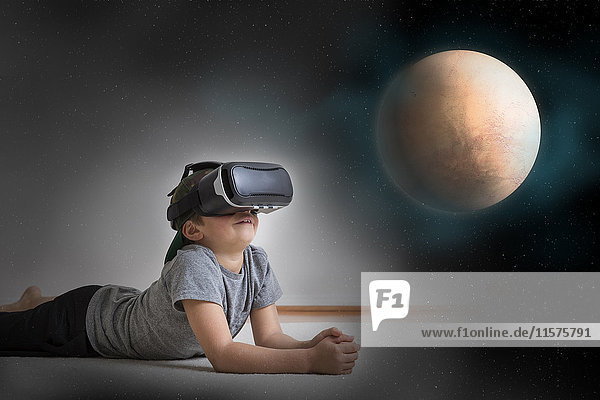 Junge liegt auf dem Boden  trägt ein Virtual-Reality-Headset  schaut auf den Planeten  digitales Komposit