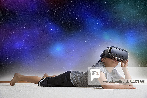 Junge liegt auf dem Boden  trägt ein Virtual-Reality-Headset  schaut in den Nachthimmel  digitales Komposit
