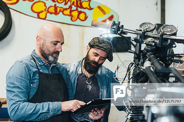 Zwei reife Männer  die in einer Garage arbeiten und ein digitales Tablett benutzen
