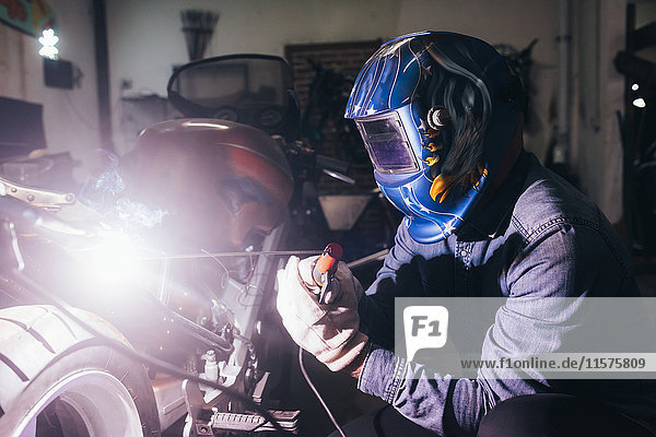 Älterer Mann in der Garage  arbeitet am Motorrad  benutzt Schweißgeräte