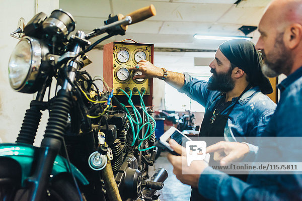 Zwei reife Männer  die in der Garage auf einem Motorrad arbeiten