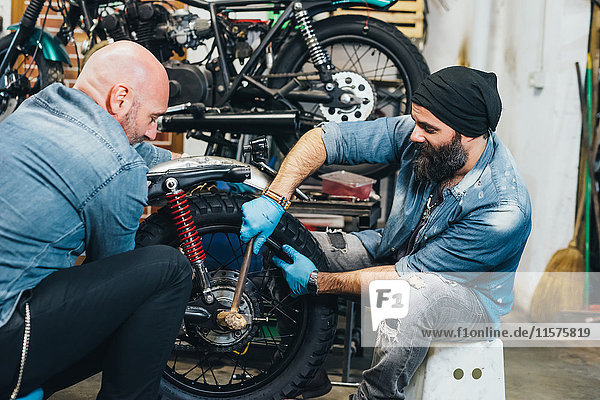 Zwei reife Männer  die in der Garage auf einem Motorrad arbeiten
