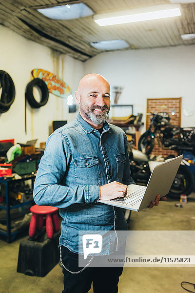 Portrait of mature man  working in garage  using laptop