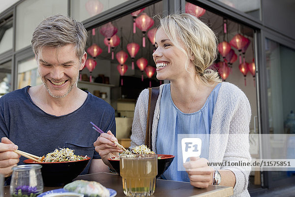 Couple eating noodles at city sidewalk cafe