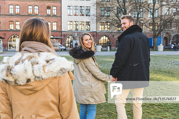Young couple looking back at friend in city