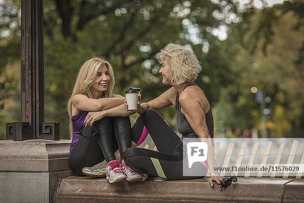 Zwei reife Freundinnen trainieren im Park  sitzen mit Kaffee zum Mitnehmen an der Wand