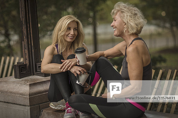 Zwei reife Freundinnen trainieren im Park  sitzen mit Kaffee zum Mitnehmen an der Wand