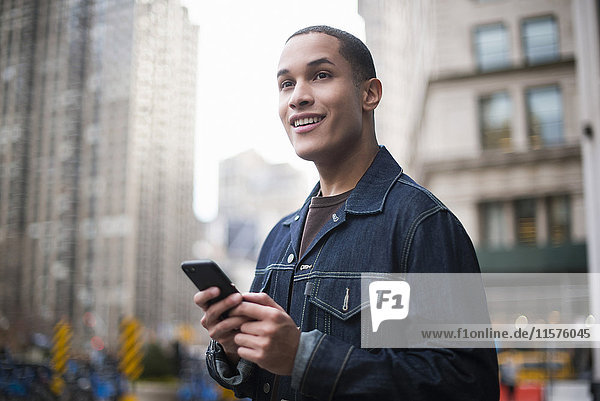 Young man standing in street  using smartphone  Manhattan  New York  USA