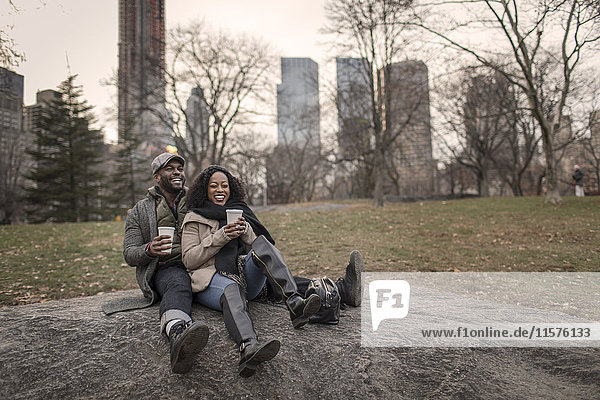 Couple sitting on rock in park with takeaway coffee
