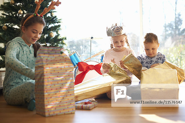Junge und Schwestern sitzen auf dem Wohnzimmerboden und öffnen Weihnachtsgeschenke